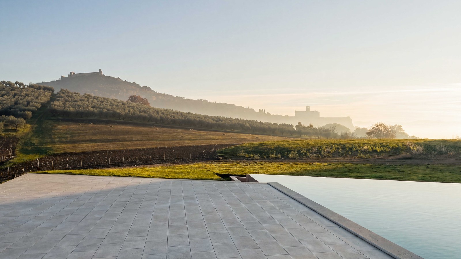 Vineyards and pool terrace of Agriturismo Alma at dawn, Assisi veiled in mist beyond